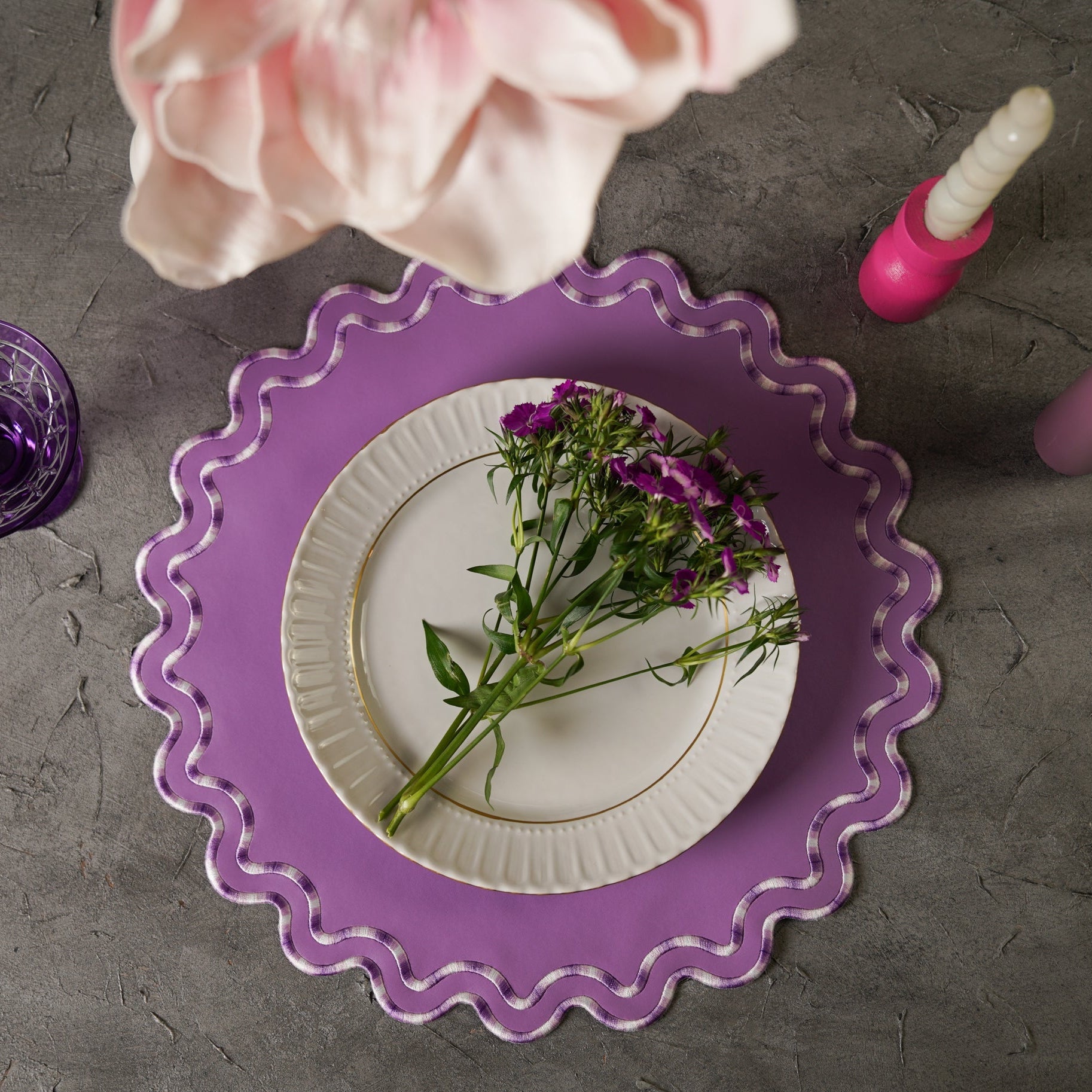 Purple decorative plate with a white plate featuring flowers on a gray surface.