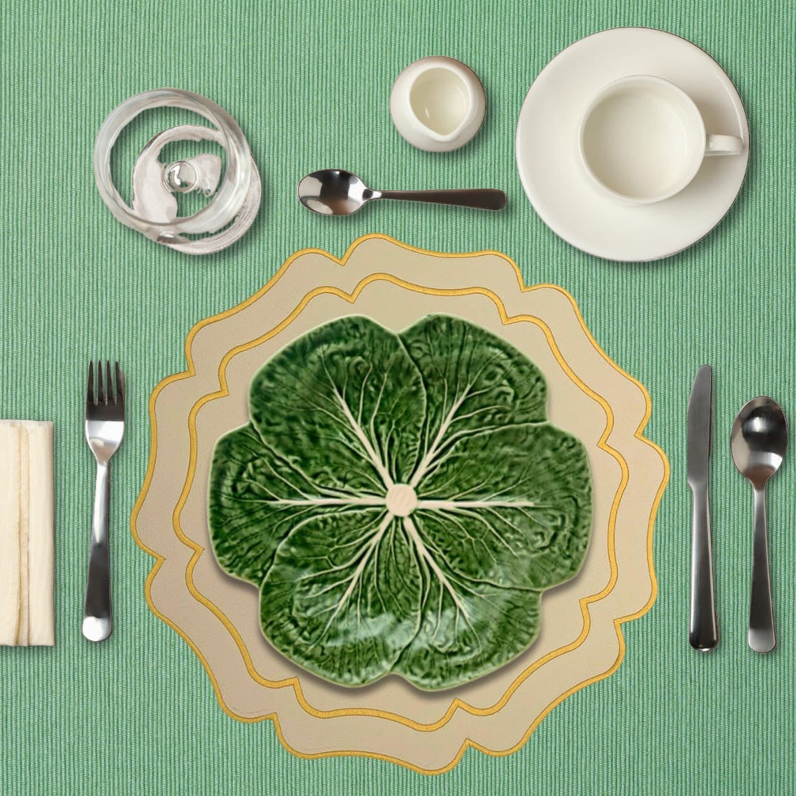 Cabbage leaf-shaped plate on a green tablecloth with silverware and cups.