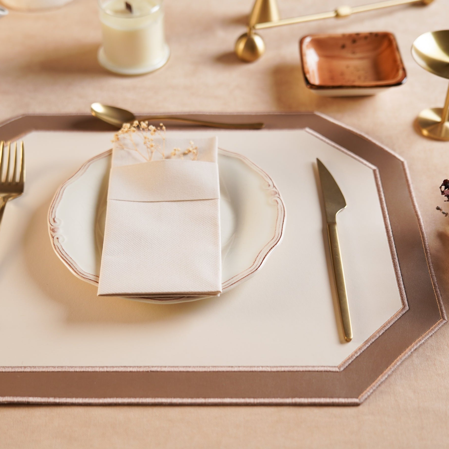 Dinner setting with a decorative placemat, plate, fork, knife, and napkin on a table.