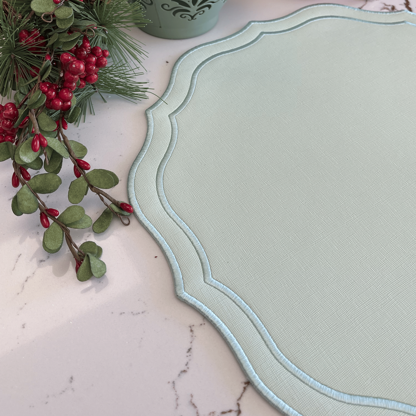 Decorative green tray with a lantern, berries, and greenery on a marble surface