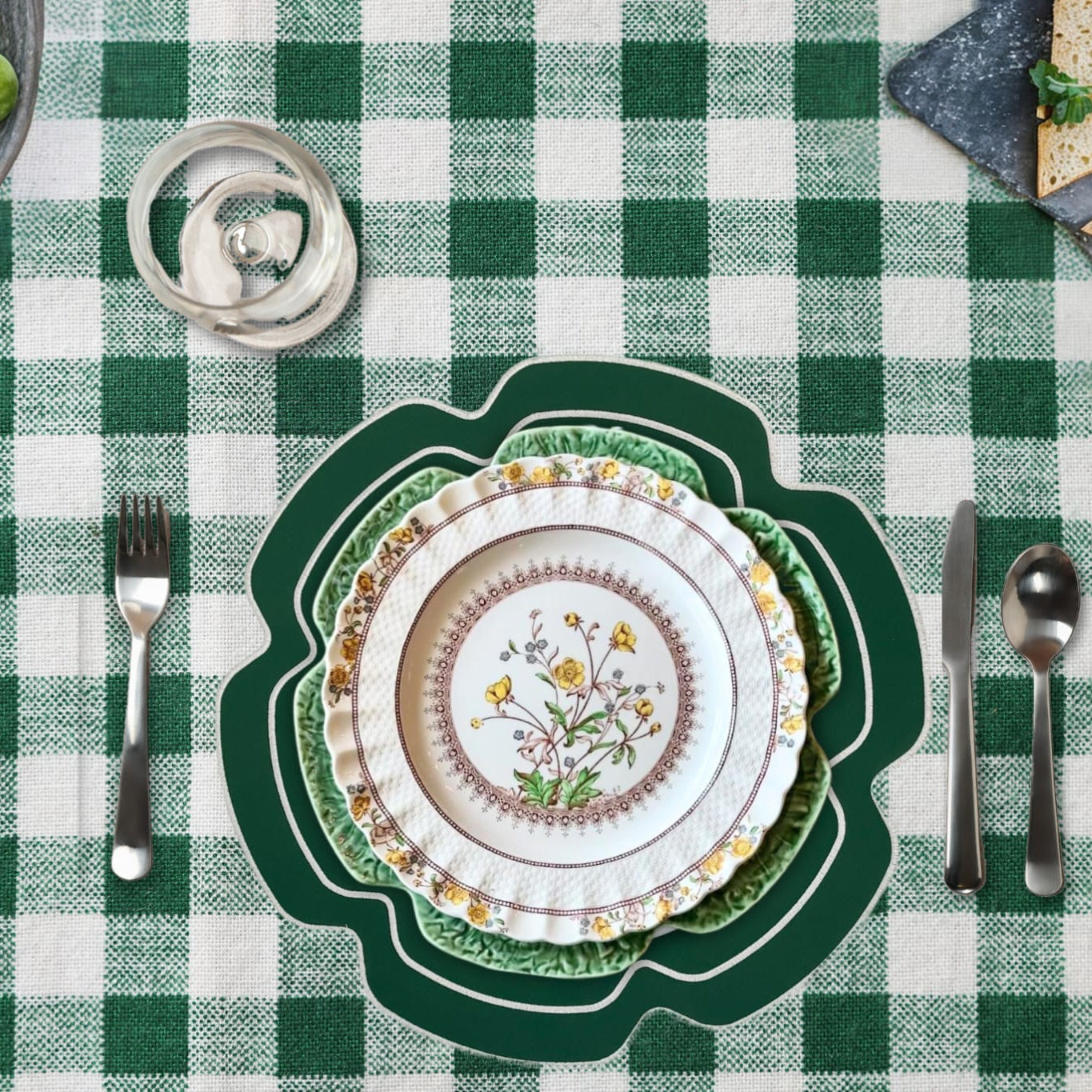 Table setting with a decorative plate, cutlery, and brussels sprouts on a green and white checkered tablecloth.