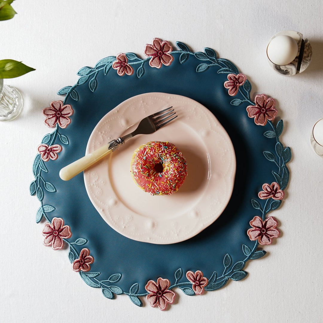 Decorative plate with floral rim, donut, and fork on a white surface with flowers.