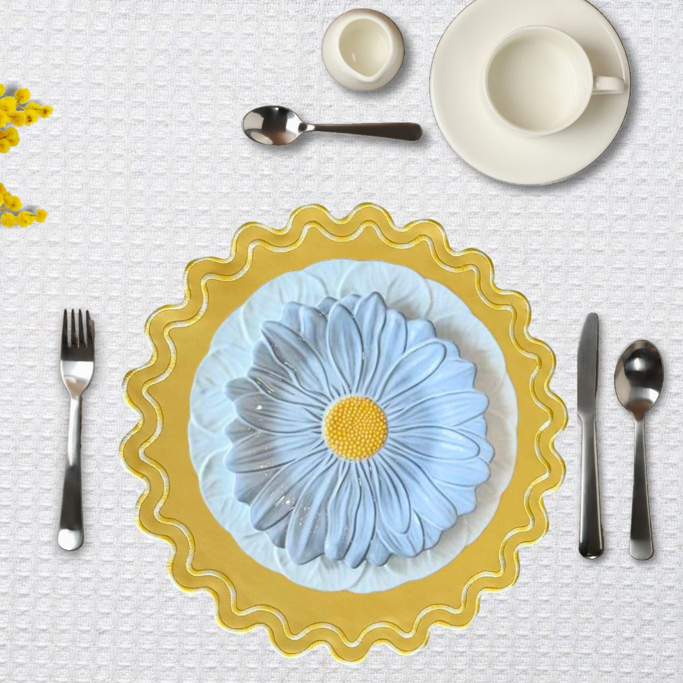 A round placemat with a yellow border and a white floral pattern in the center, presented on a table setting with cutlery and a cup.