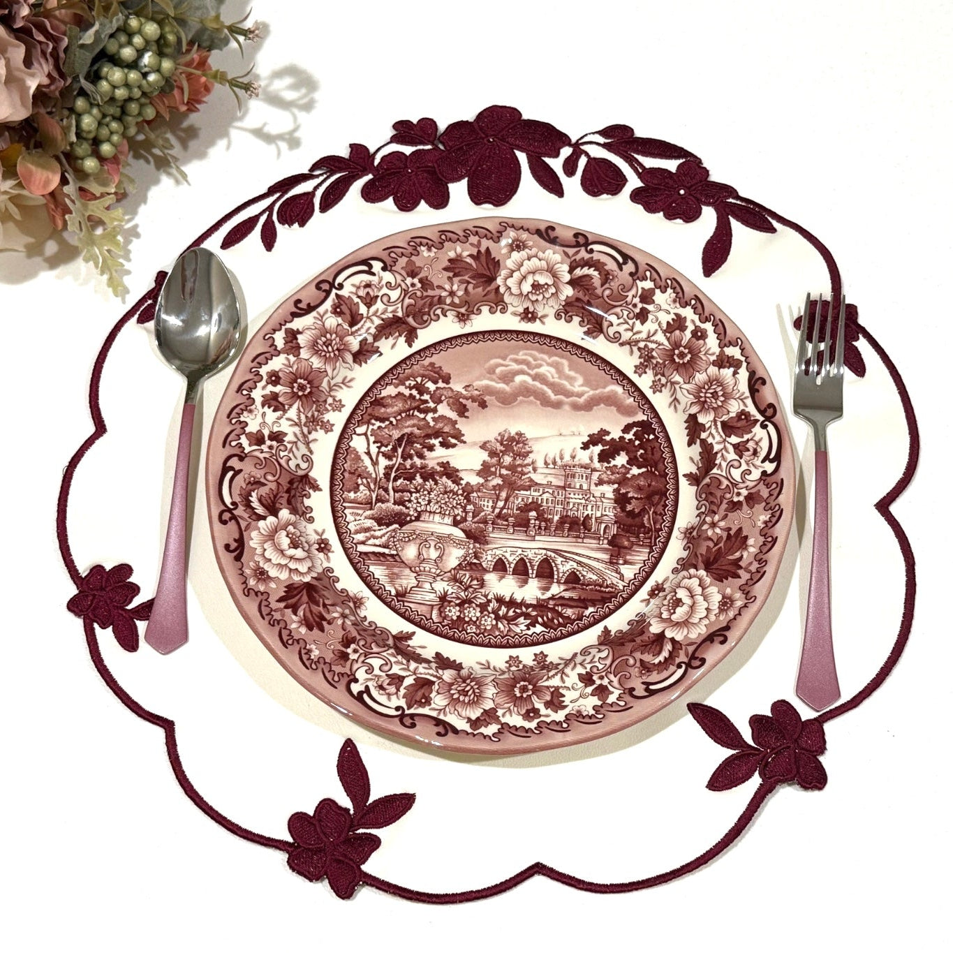 A set of round faux leather placemats with floral embroidery around the edge, displayed with a plate and cutlery in the center.