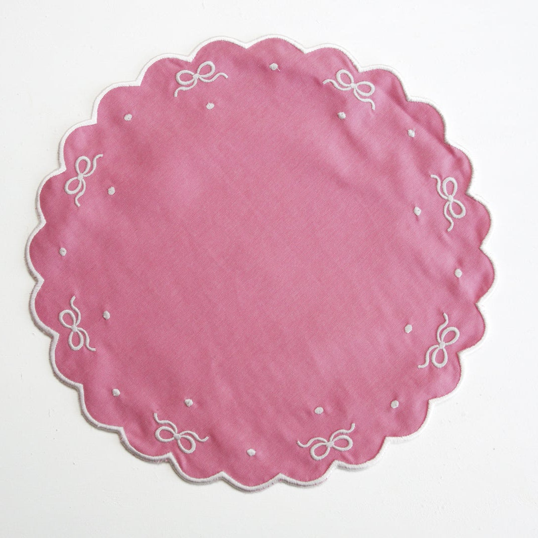 Pink paper plate with white decorative bows on a light gray background