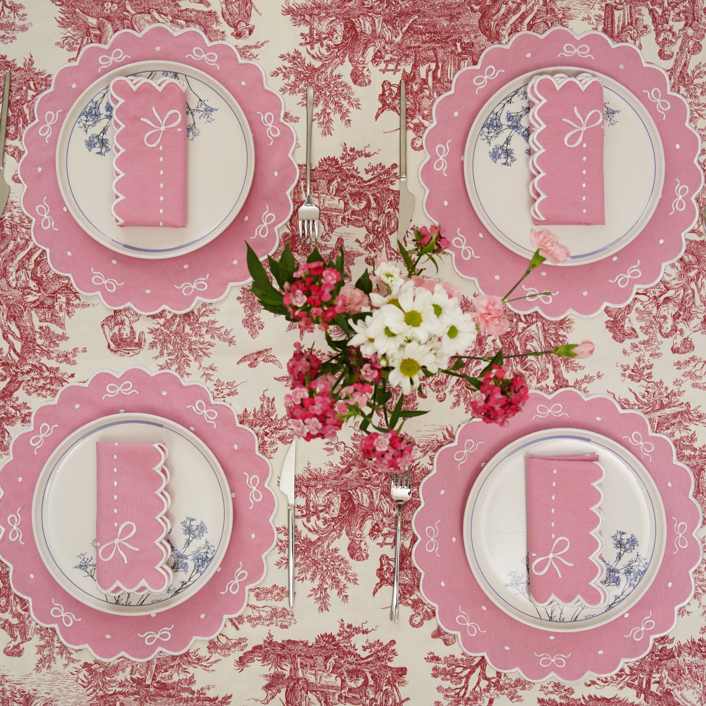 Table setting with pink plates and napkins on a floral tablecloth