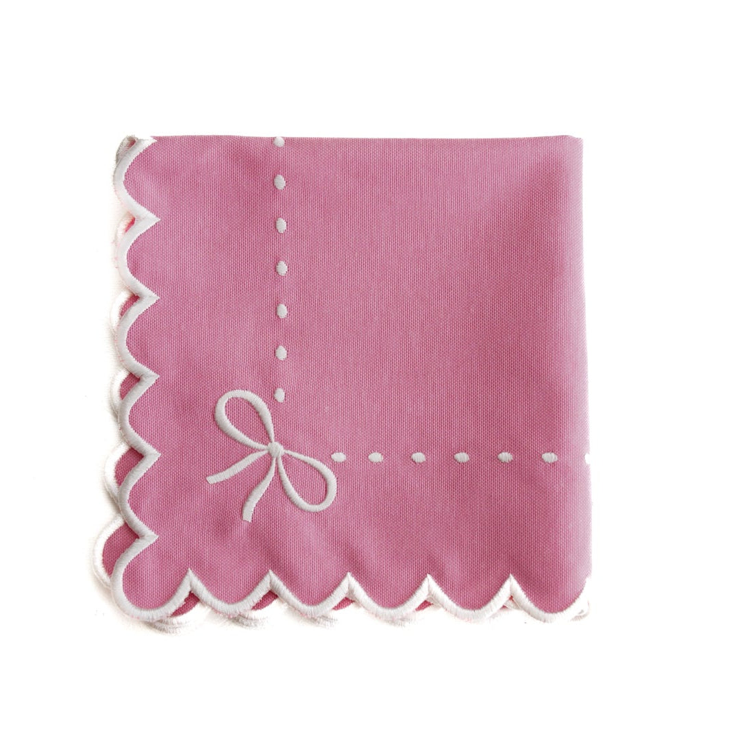 Pink napkin with scalloped edge and white bow design on a white background
