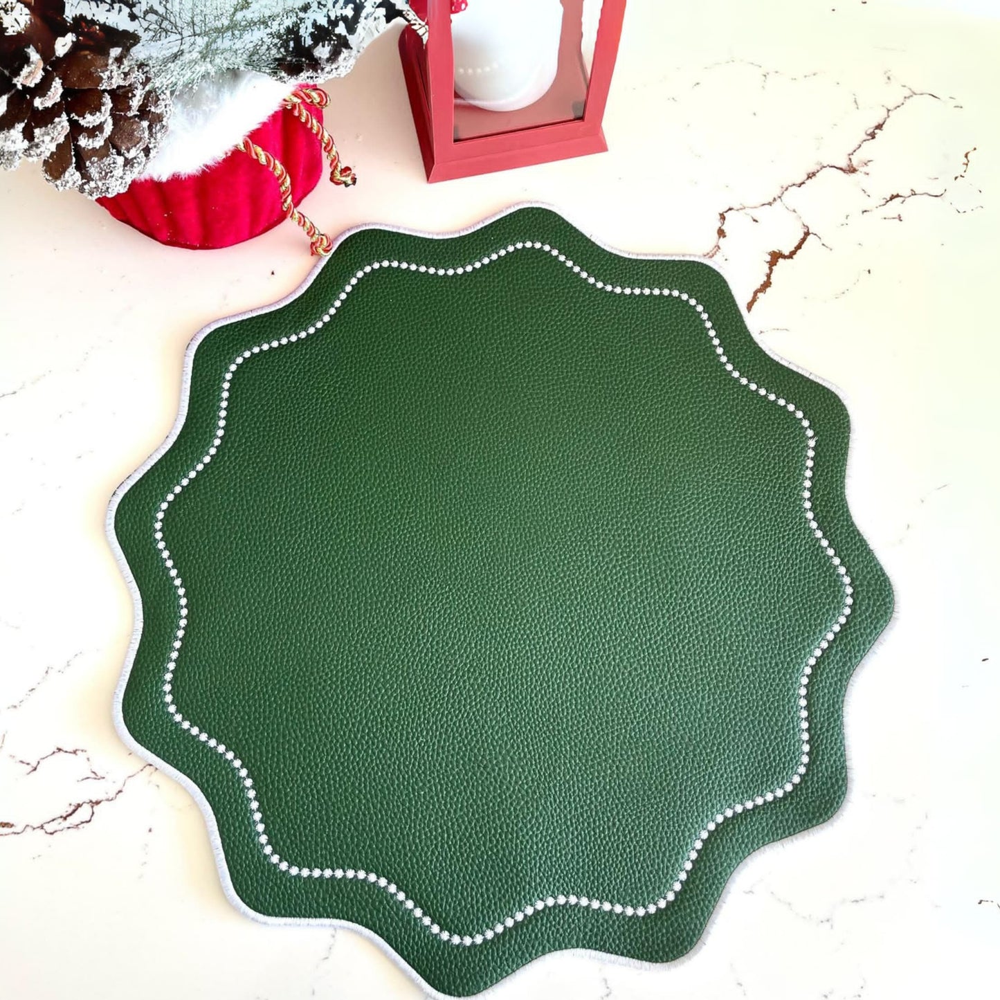 A round green faux leather placemat with white stitching around the edge, placed on a white surface with a Christmas decoration in the background.