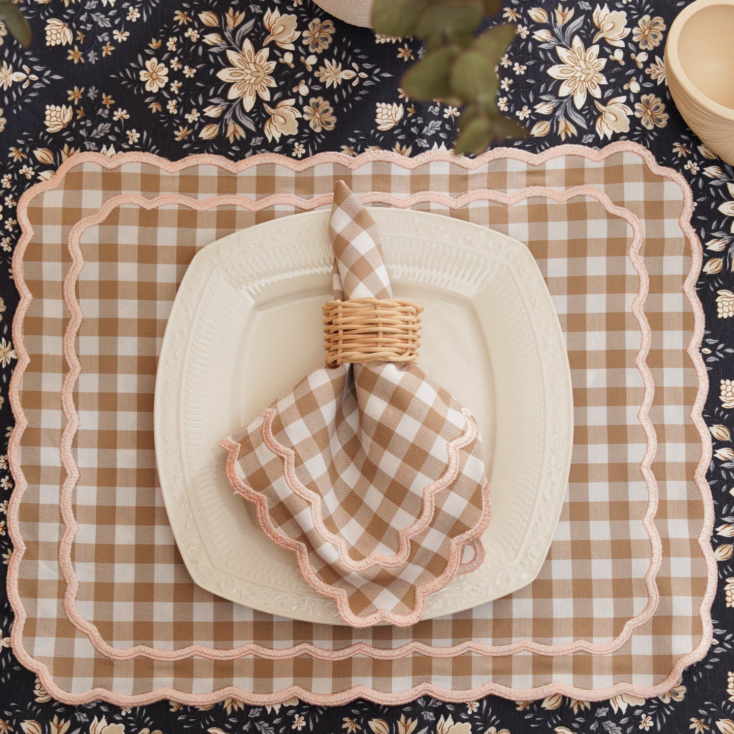 Table setting with checkered plates, napkins, and cutlery on a floral tablecloth.