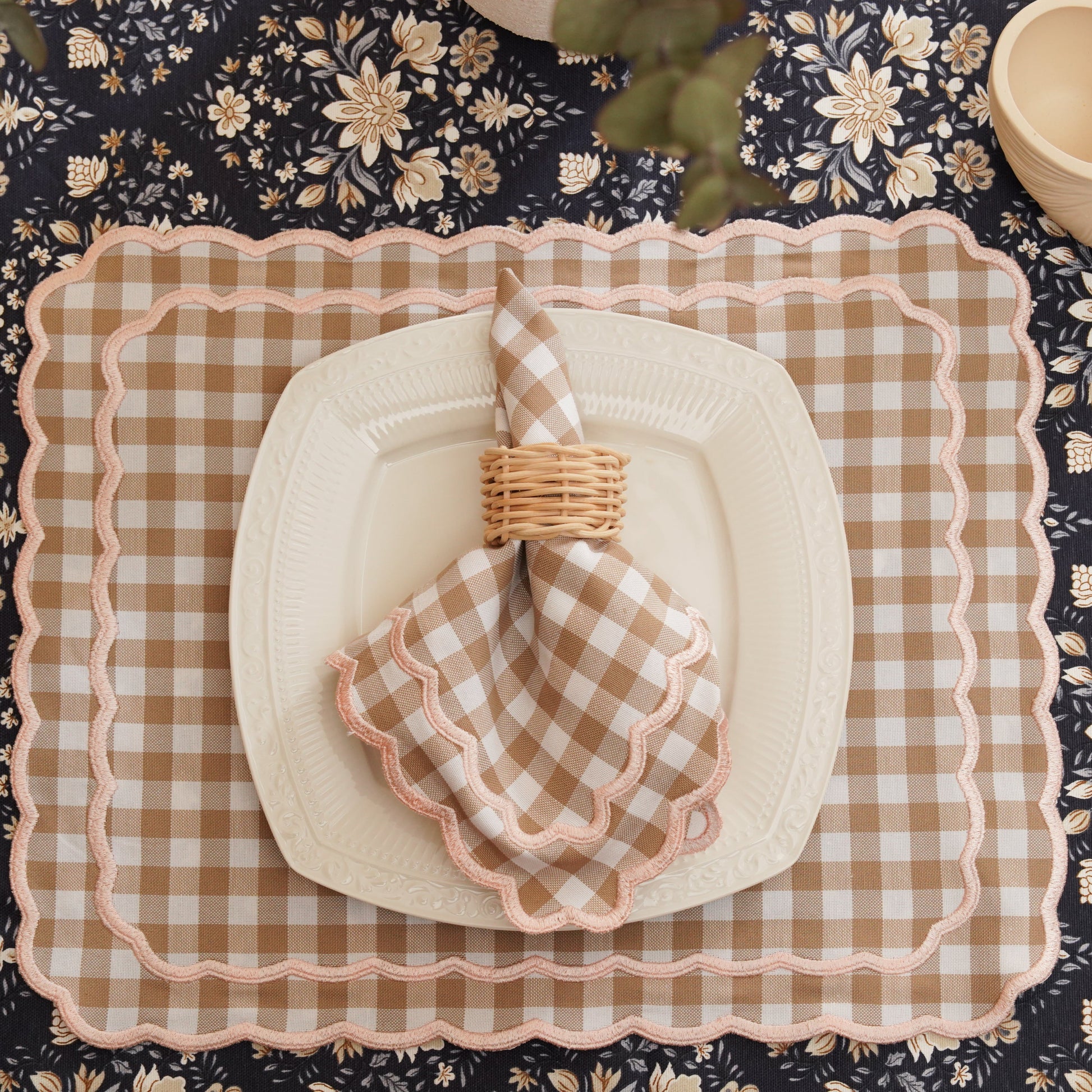 Table setting with checkered plates, napkins, and cutlery on a floral tablecloth.