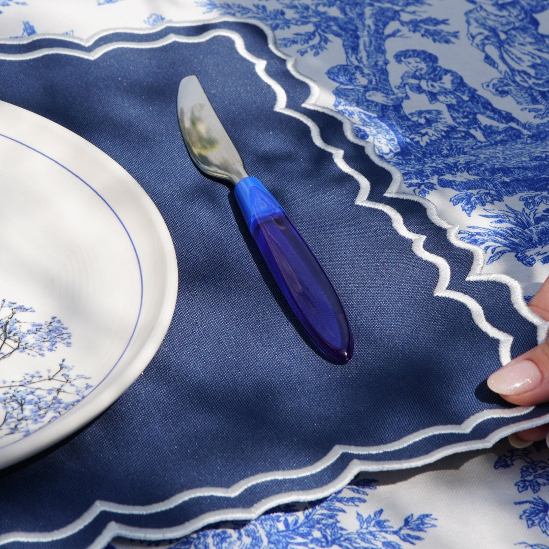 Blue and white patterned tablecloth with a plate, knife, and hand.