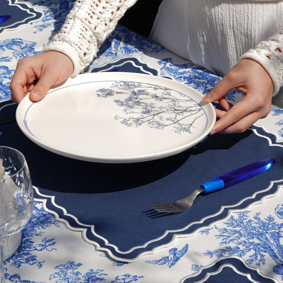 Person setting a table with blue and white patterns, including a plate and cutlery.