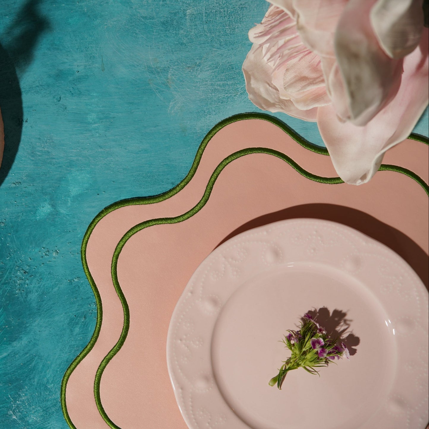 Pink flower above a white plate with a small plant on a blue and pink textured background