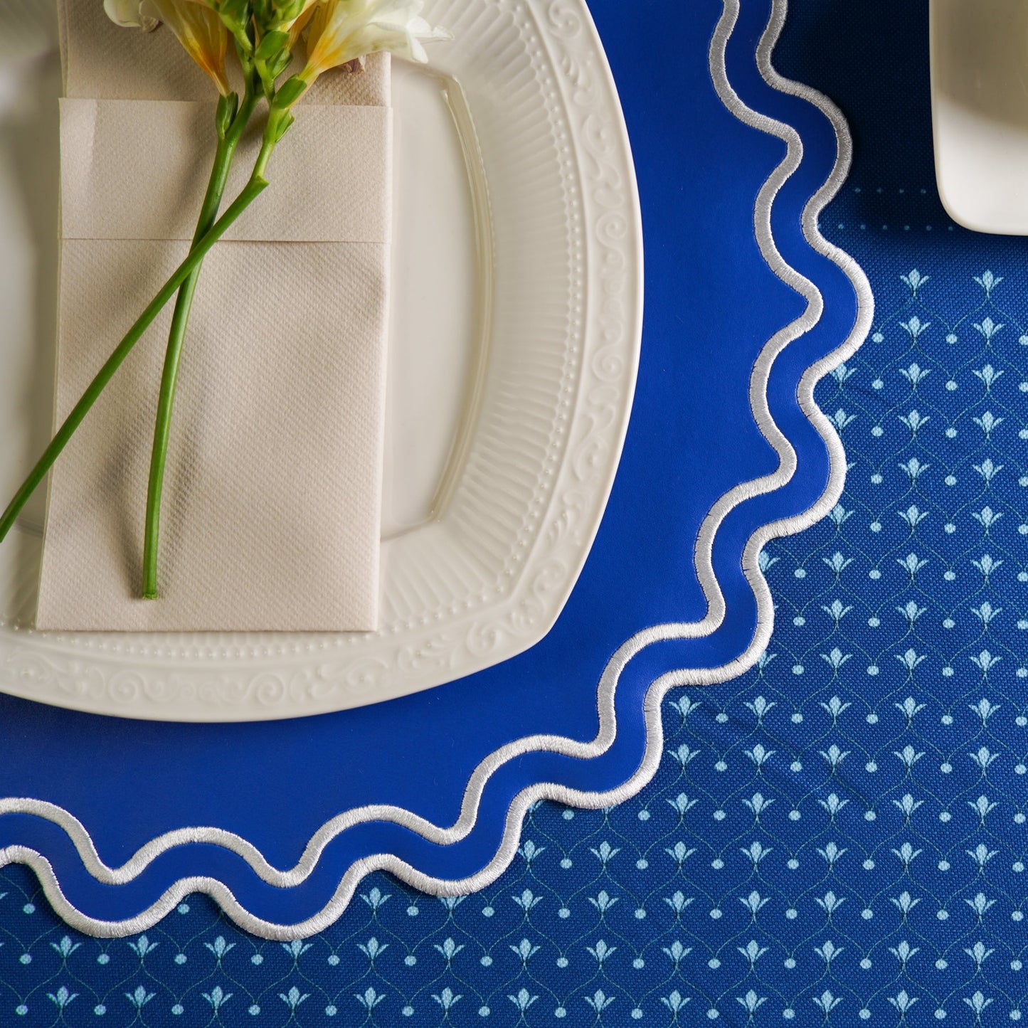 White plate with a folded napkin and flower on a blue patterned tablecloth