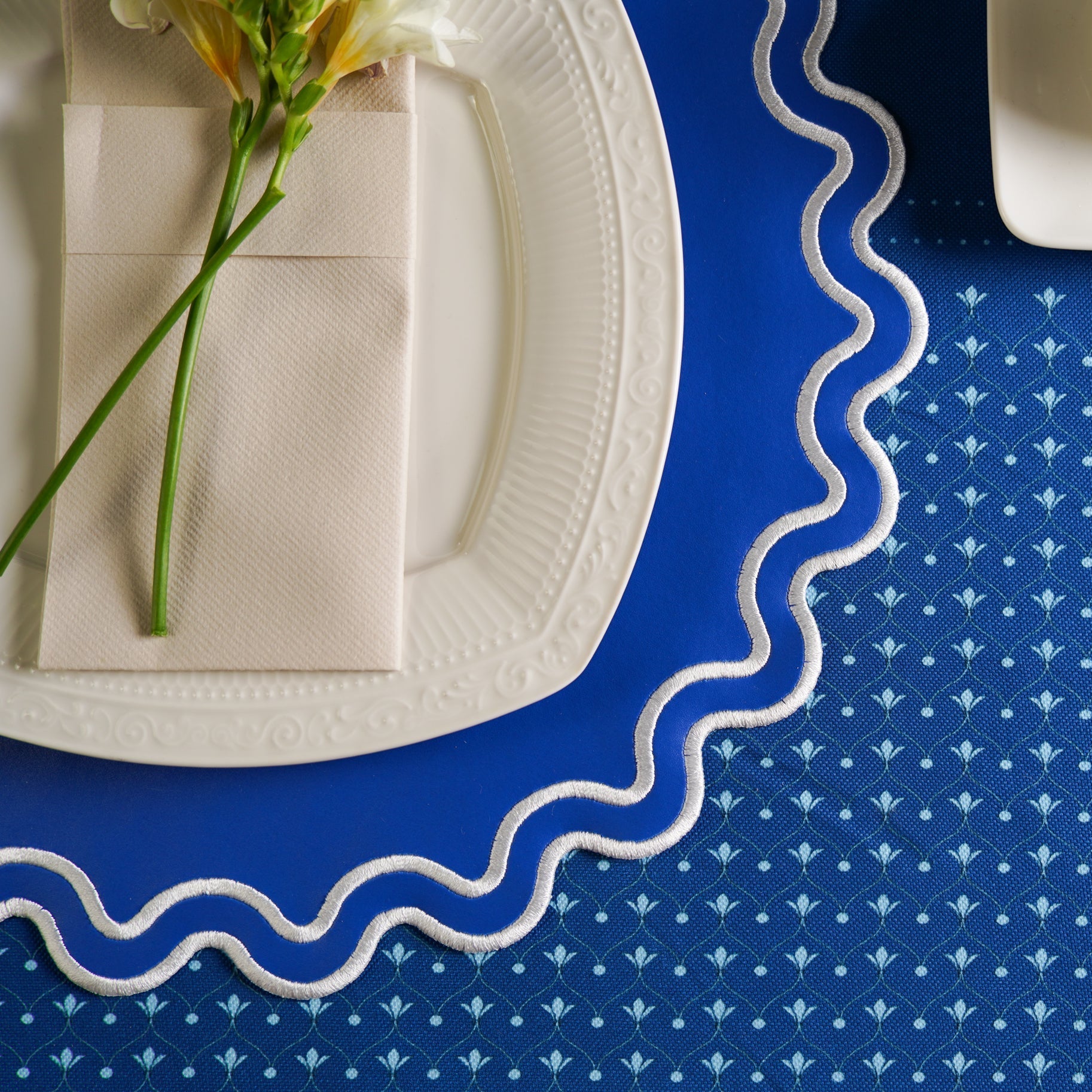 White plate with a folded napkin and flower on a blue patterned tablecloth