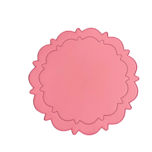 A round pink faux leather placemat with a scalloped edge design.