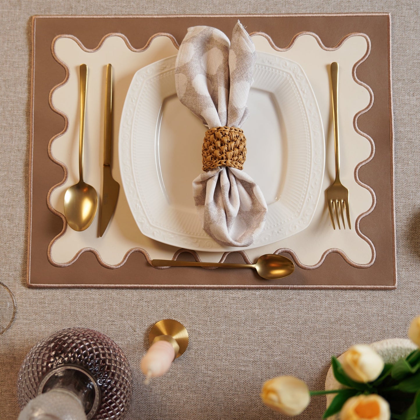 Elegant table setting with a white plate, gold cutlery, and decorative napkin on a textured surface.