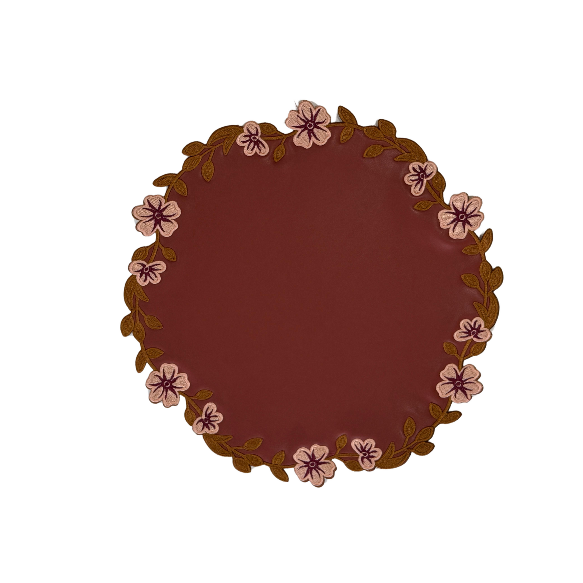 Round dark orange faux leather placemat with a floral pattern around the edge.