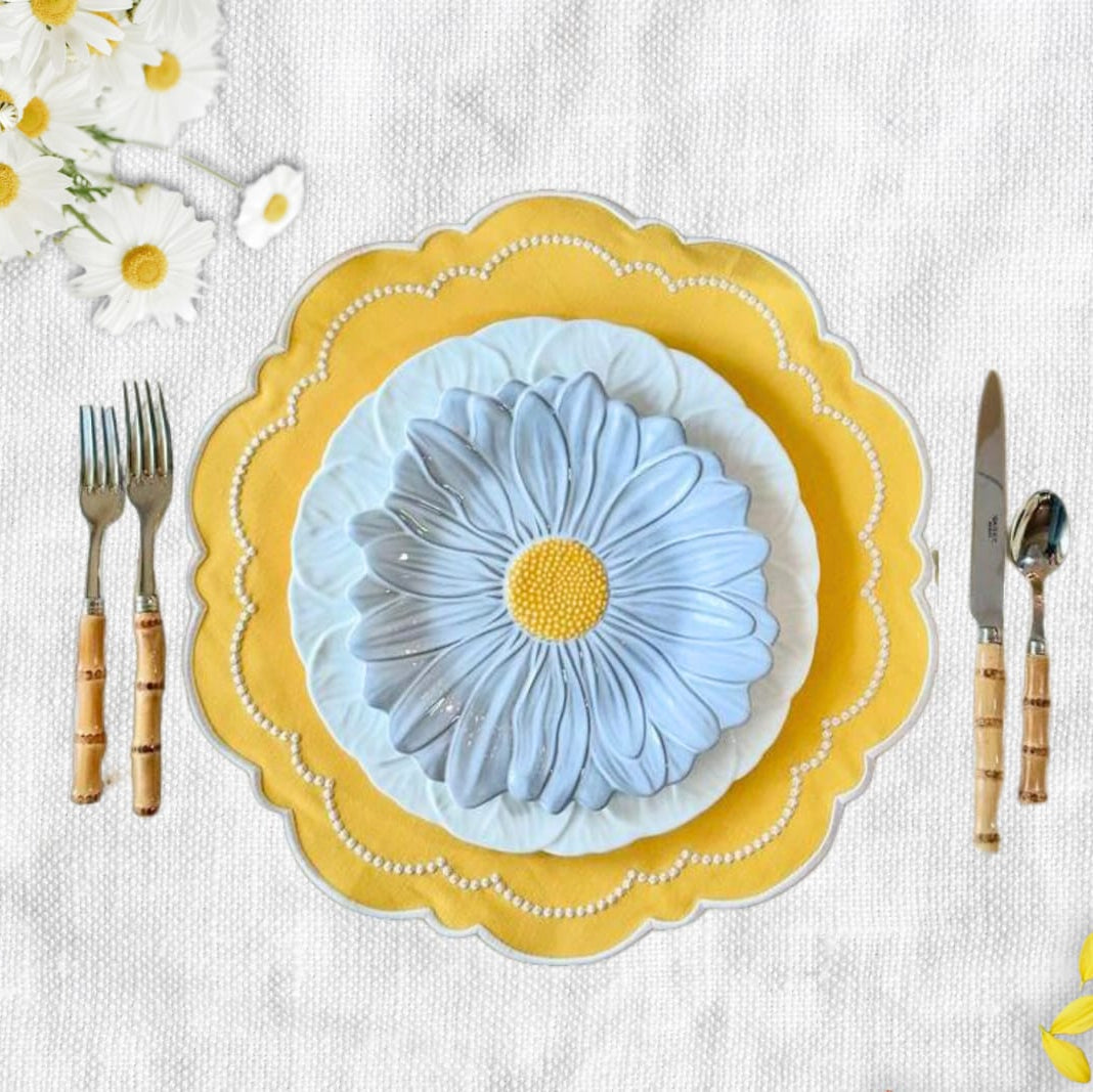 A set table with a yellow floral patterned placemat, white plate, and silverware.