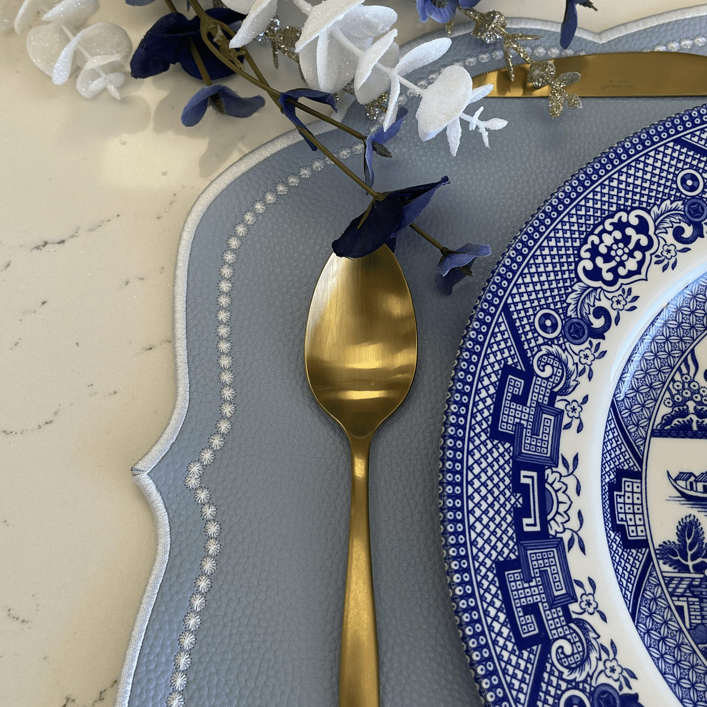 Dinner setting with blue and white plates, gold spoon, and decorative elements on a marble surface.