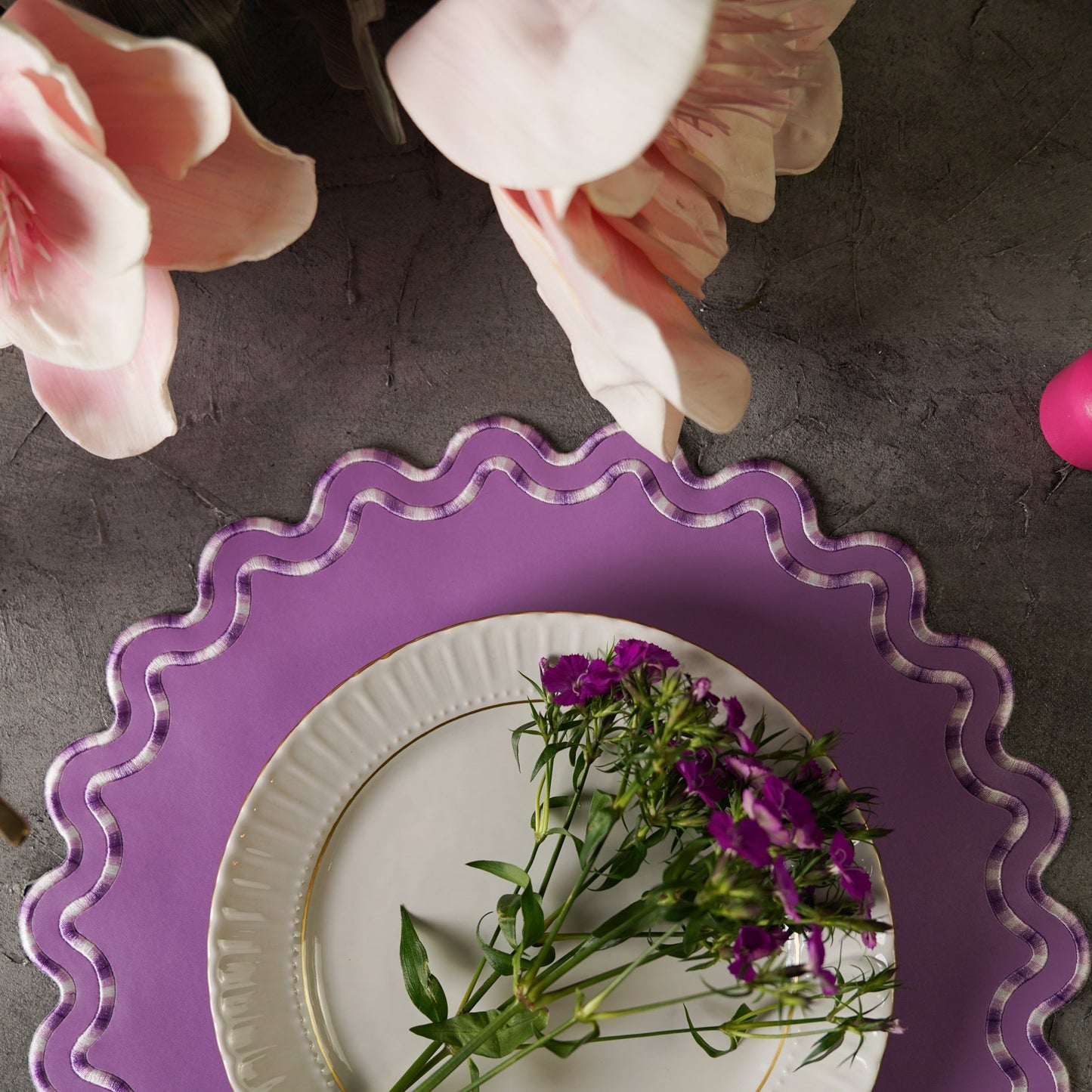 Purple decorative plate with a white plate underneath featuring purple flowers, on a dark surface.