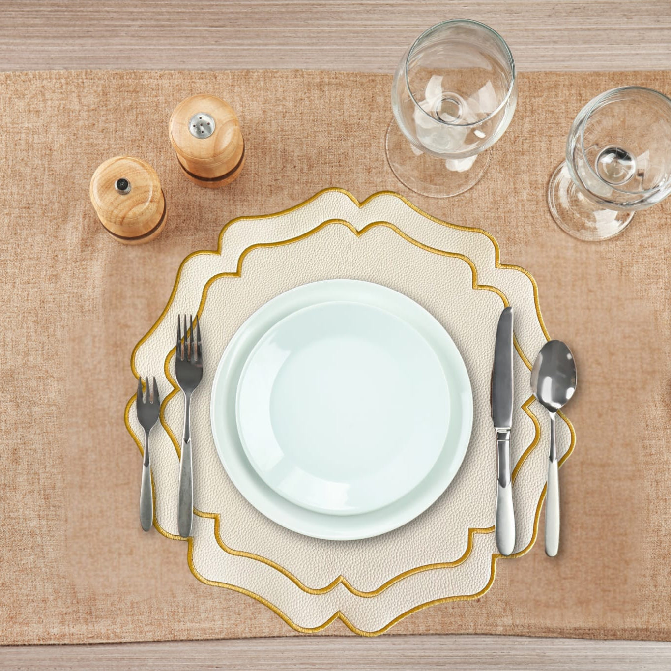 Table setting with a decorative plate, cutlery, and glasses on a textured placemat.
