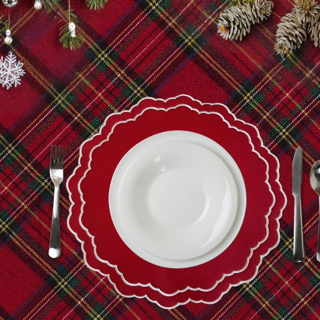 Red plaid tablecloth with a white plate, red scalloped placemat, silverware, and Christmas decorations.