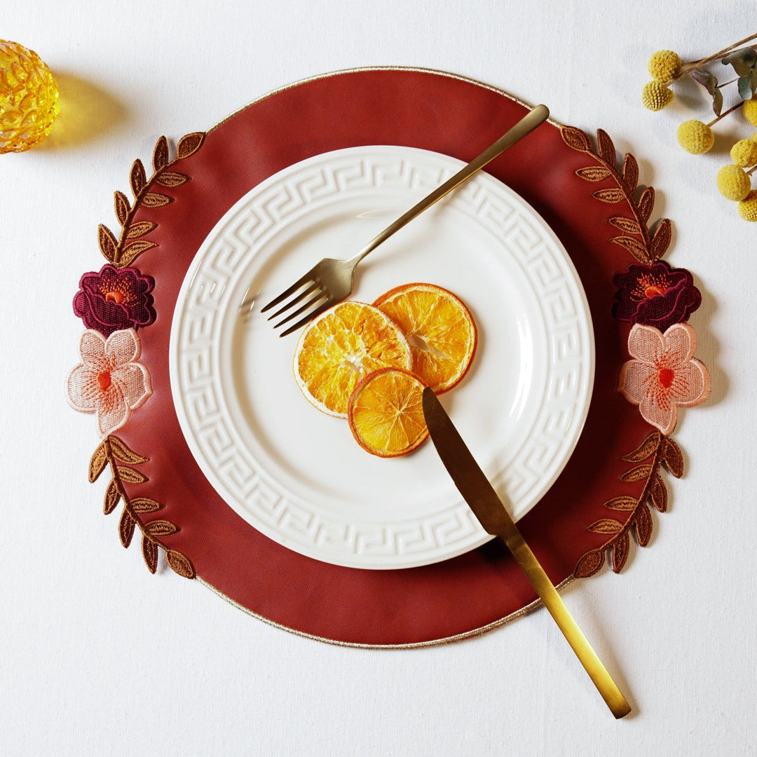 White plate with sliced oranges, gold fork and knife on a red charger plate, surrounded by decorative elements.