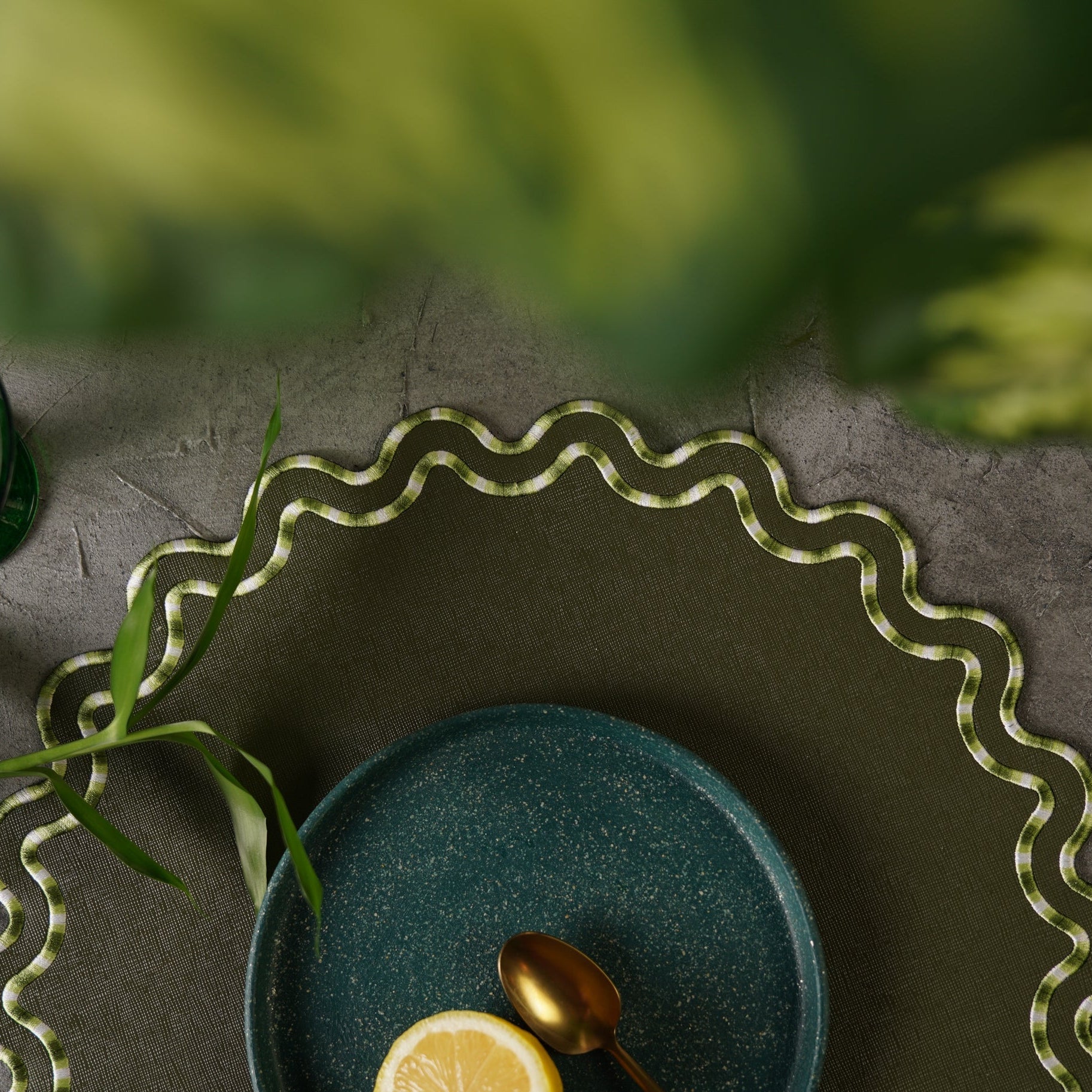 Green plate with a lemon and spoon on a textured surface with wavy edge