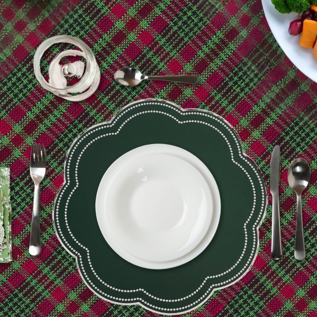 Table setting with a green plate, white bowl, and silverware on a red and green plaid tablecloth.