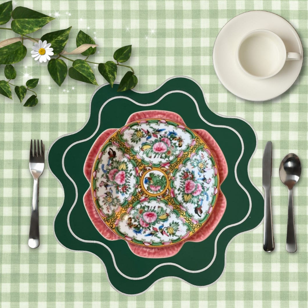 Decorative plate with floral design on a green checkered tablecloth with cutlery and a cup.