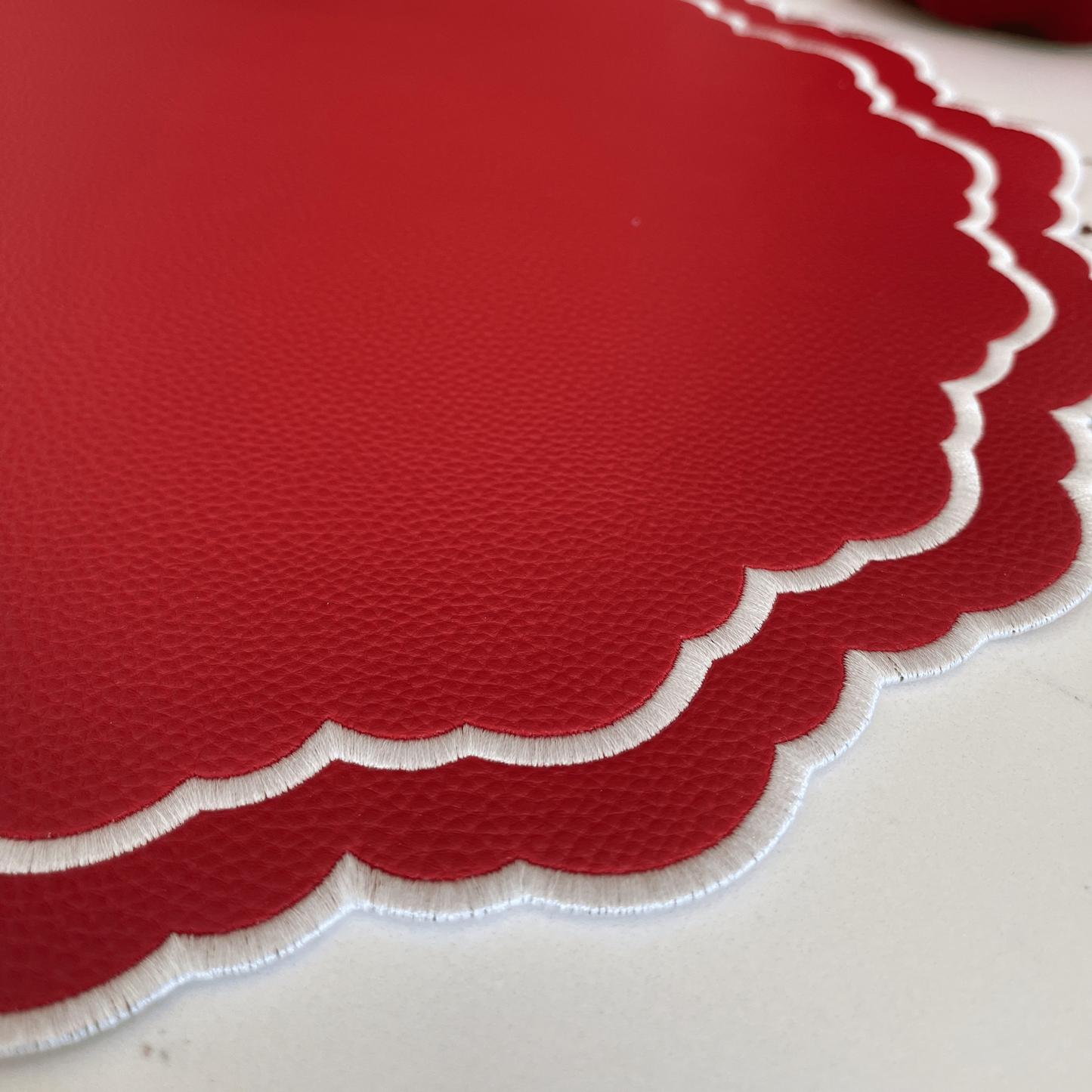 Red scalloped-edge placemat on a white surface with Christmas decorations in the background.
