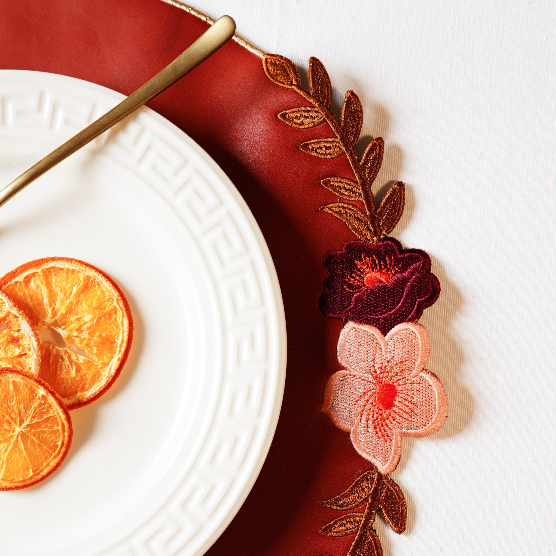 Decorative plate with floral design, dried oranges, and a gold fork on a white background