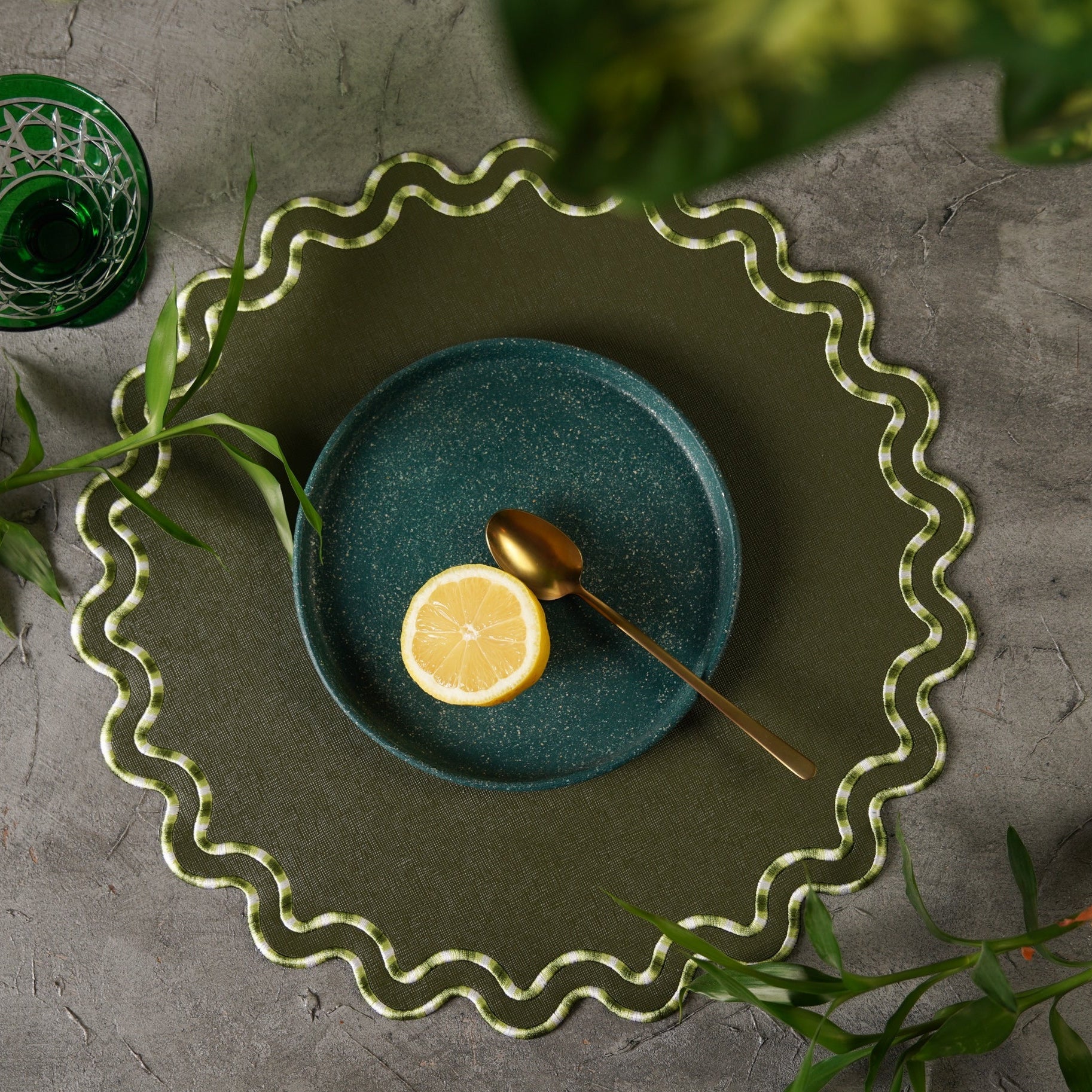 Green plate with a lemon and spoon on a textured surface with greenery