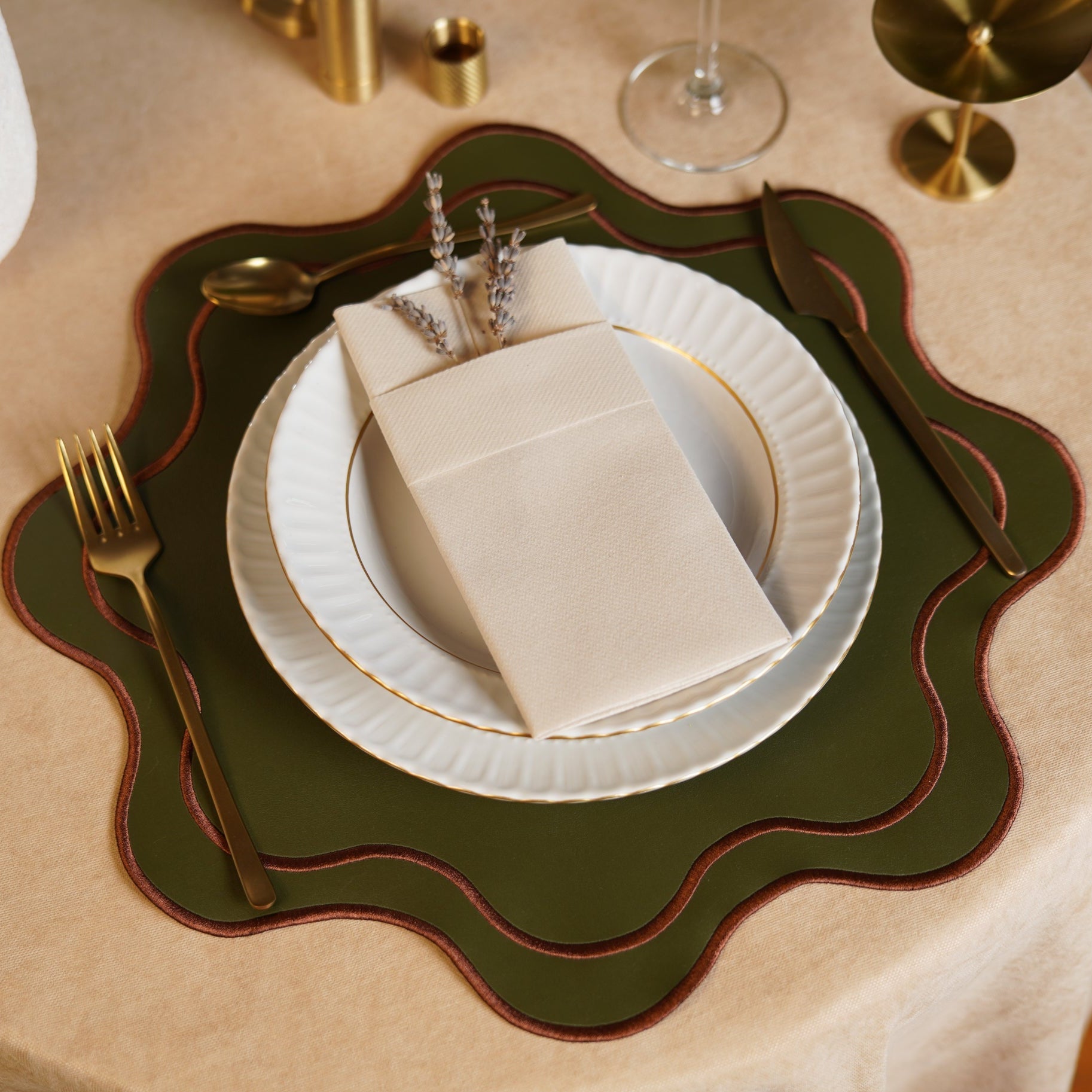Elegant table setting with a green placemat, white plates, gold cutlery, and beige napkins.
