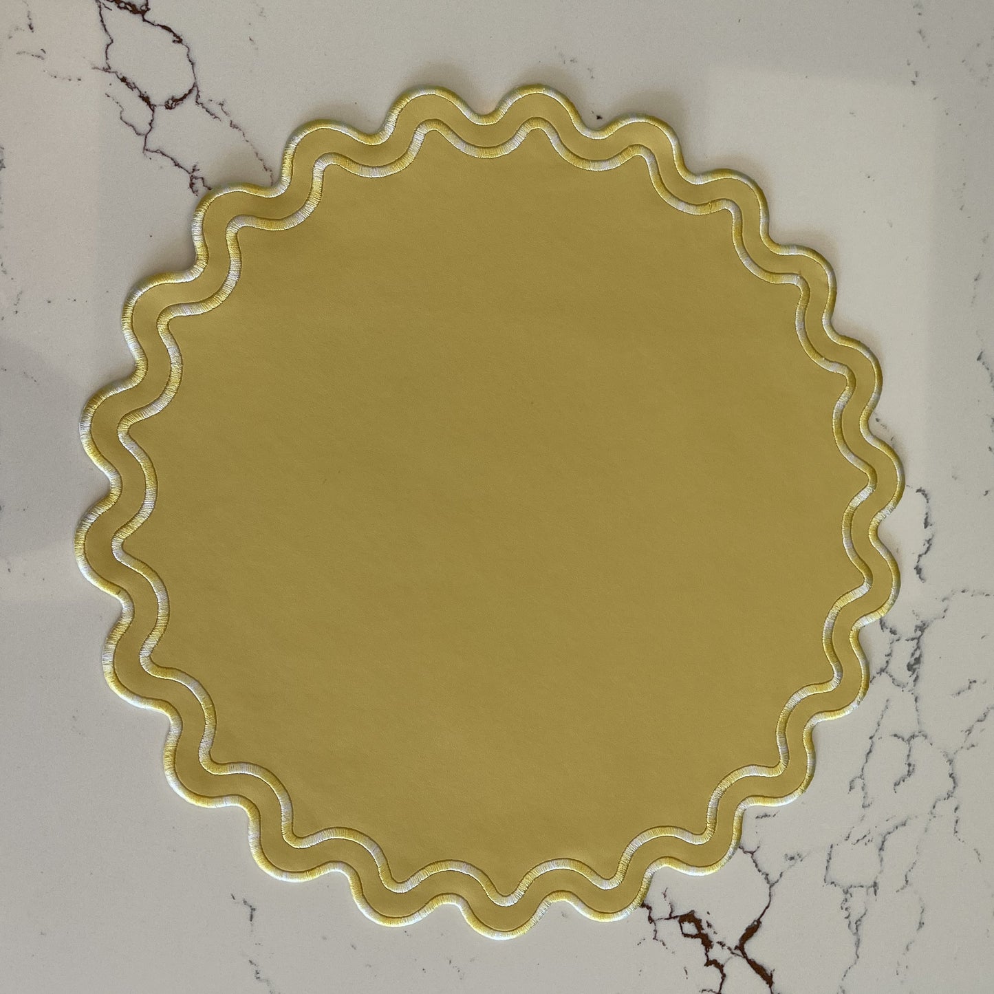 Round yellow decorative item with scalloped edge on a marble surface