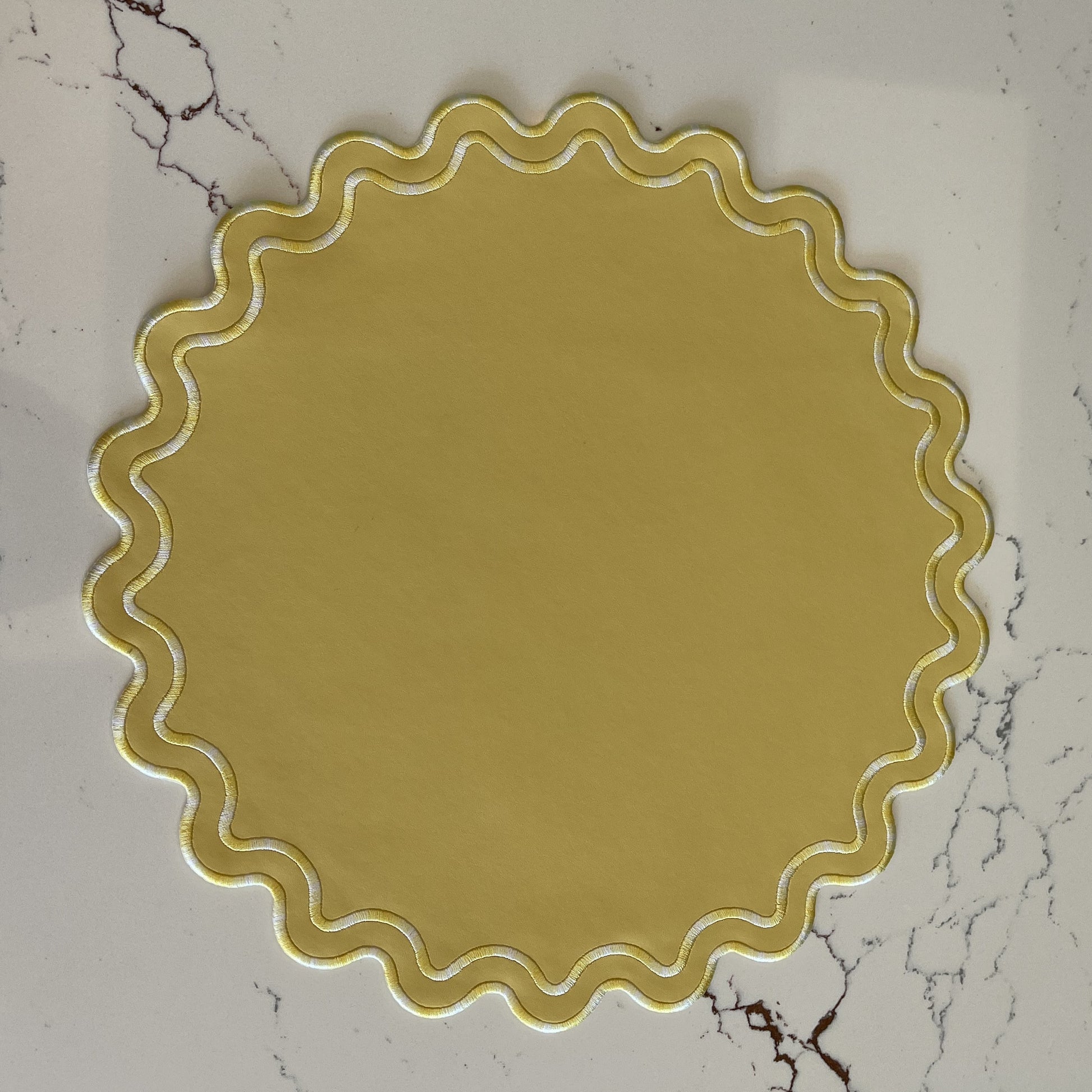 Round yellow decorative item with scalloped edge on a marble surface