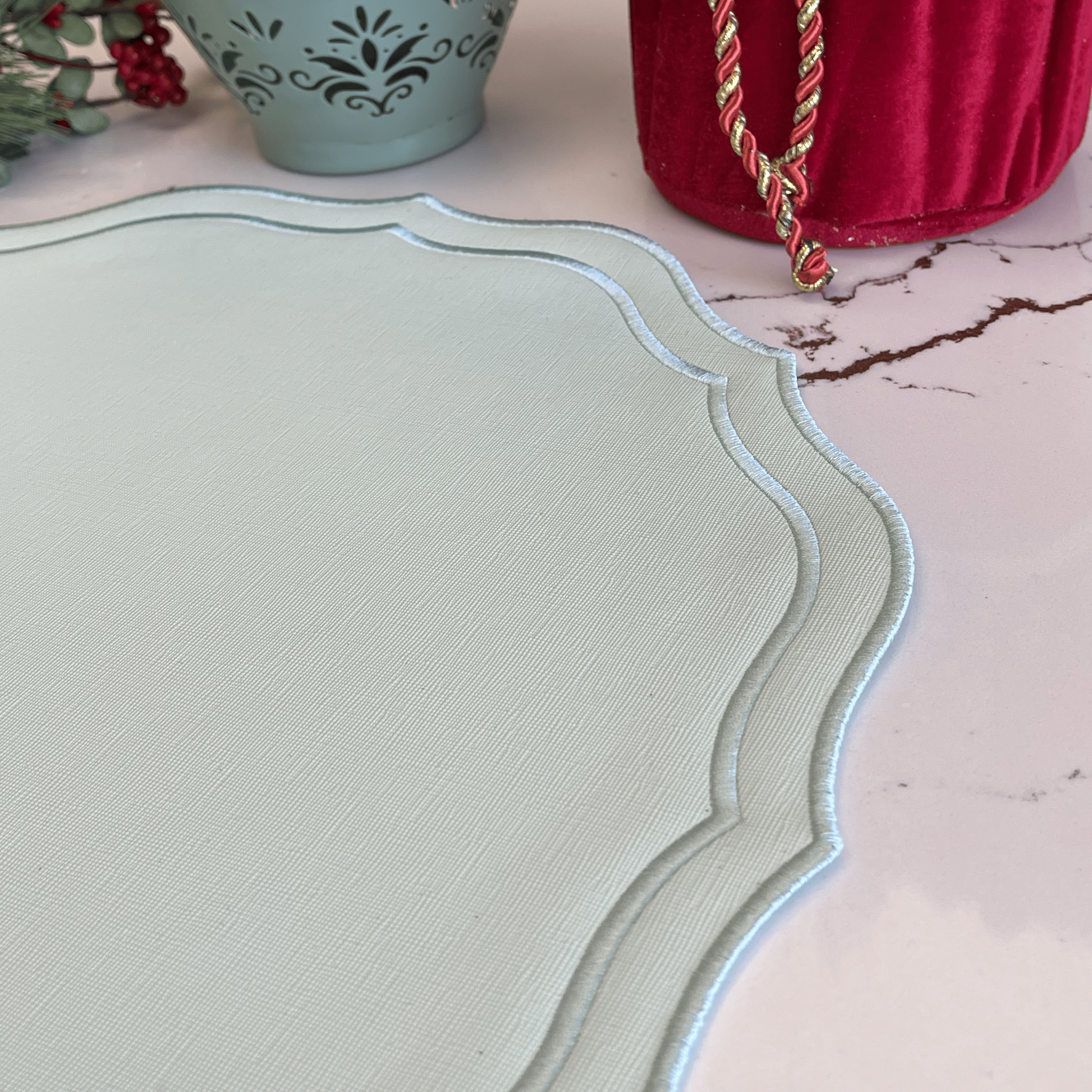 Decorative table setting with a light green placemat, decorative vase, and red bag on a pink surface.