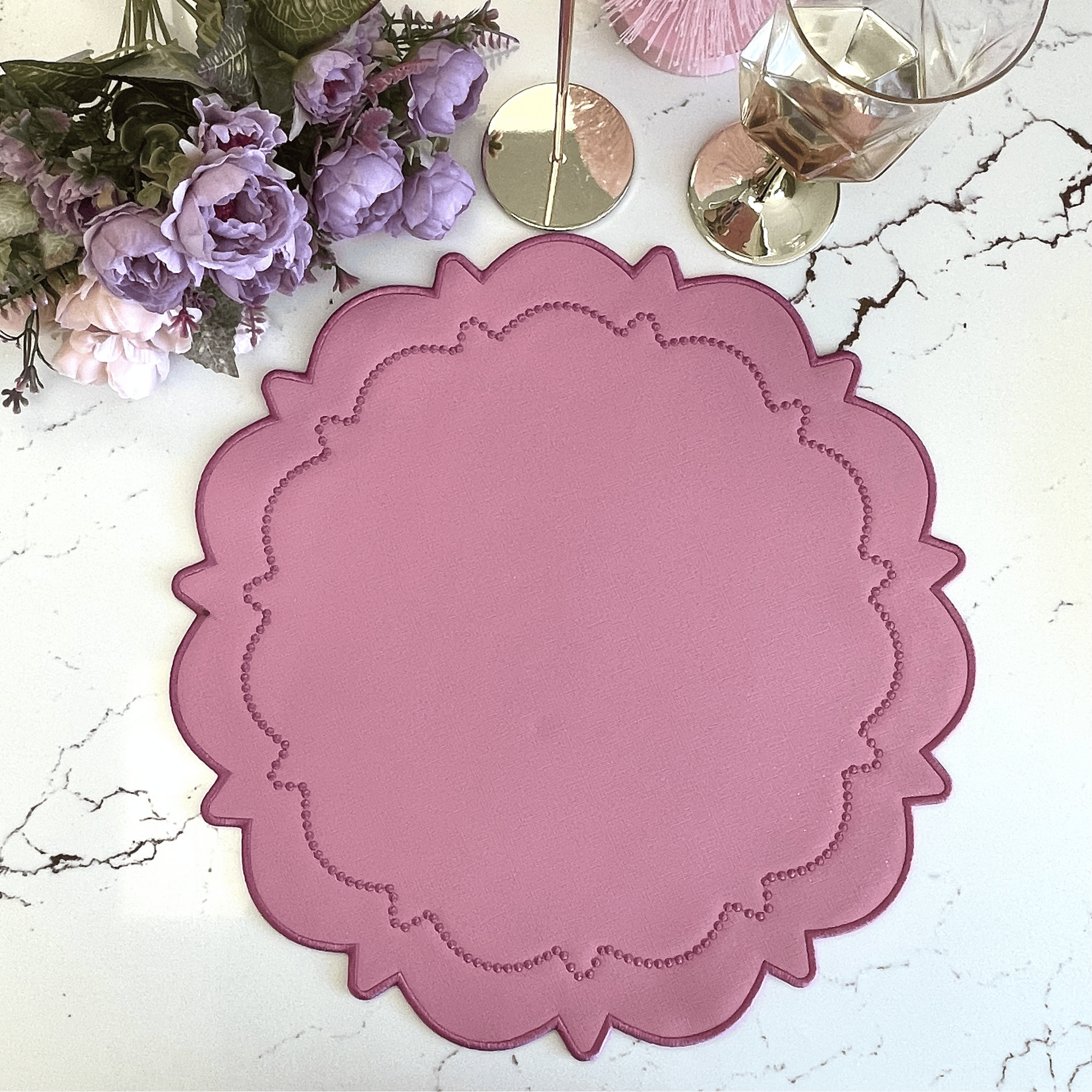 Pink decorative placemat on a marble surface with flowers and candles.