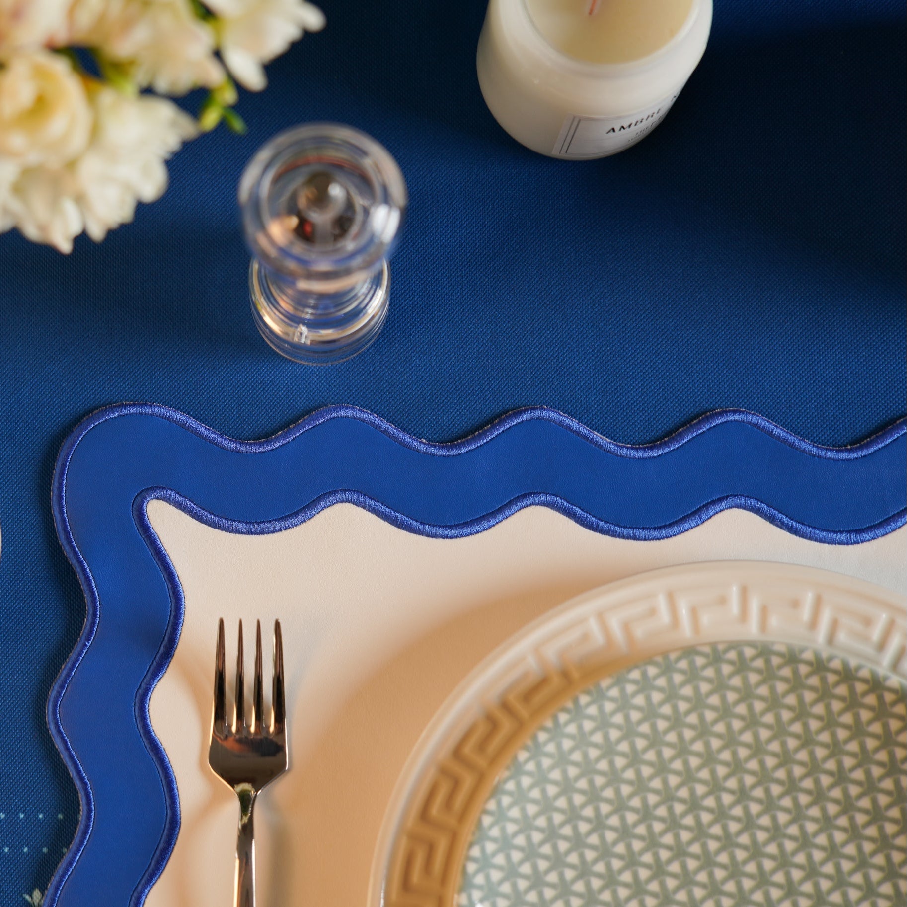 Table setting with blue placemat, white plate, silver fork, and decorative flowers.