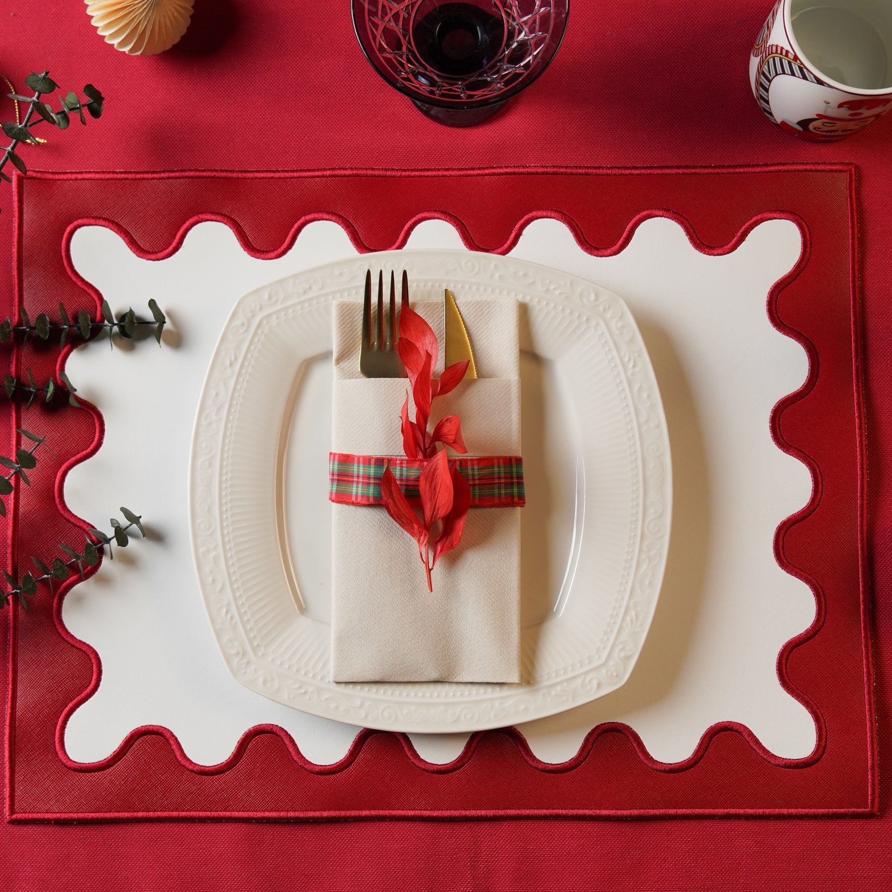Dining table setting with a red placemat, white plate, and folded napkin with a red ribbon.