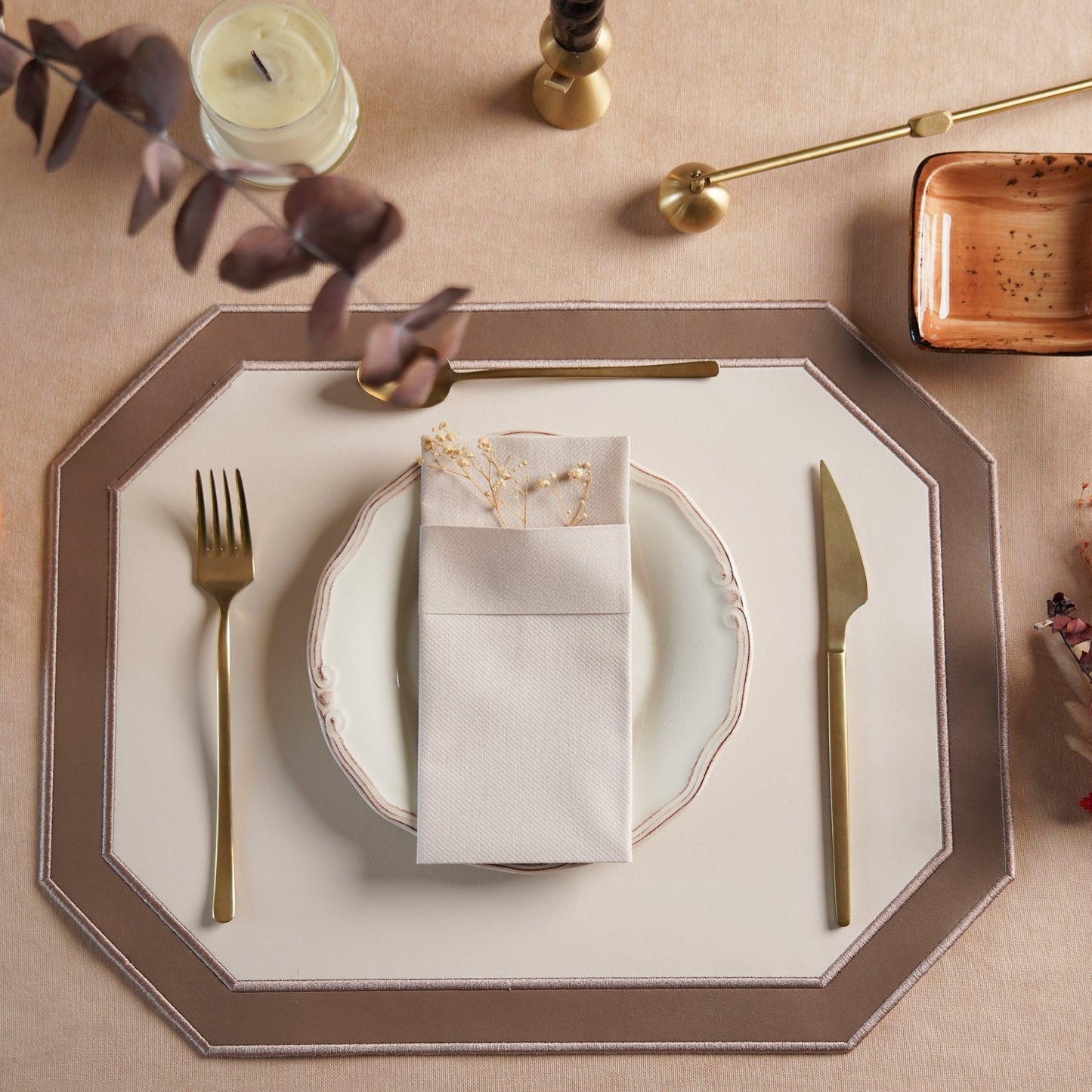 Elegant table setting with plates, cutlery, and decorative elements on a beige surface.