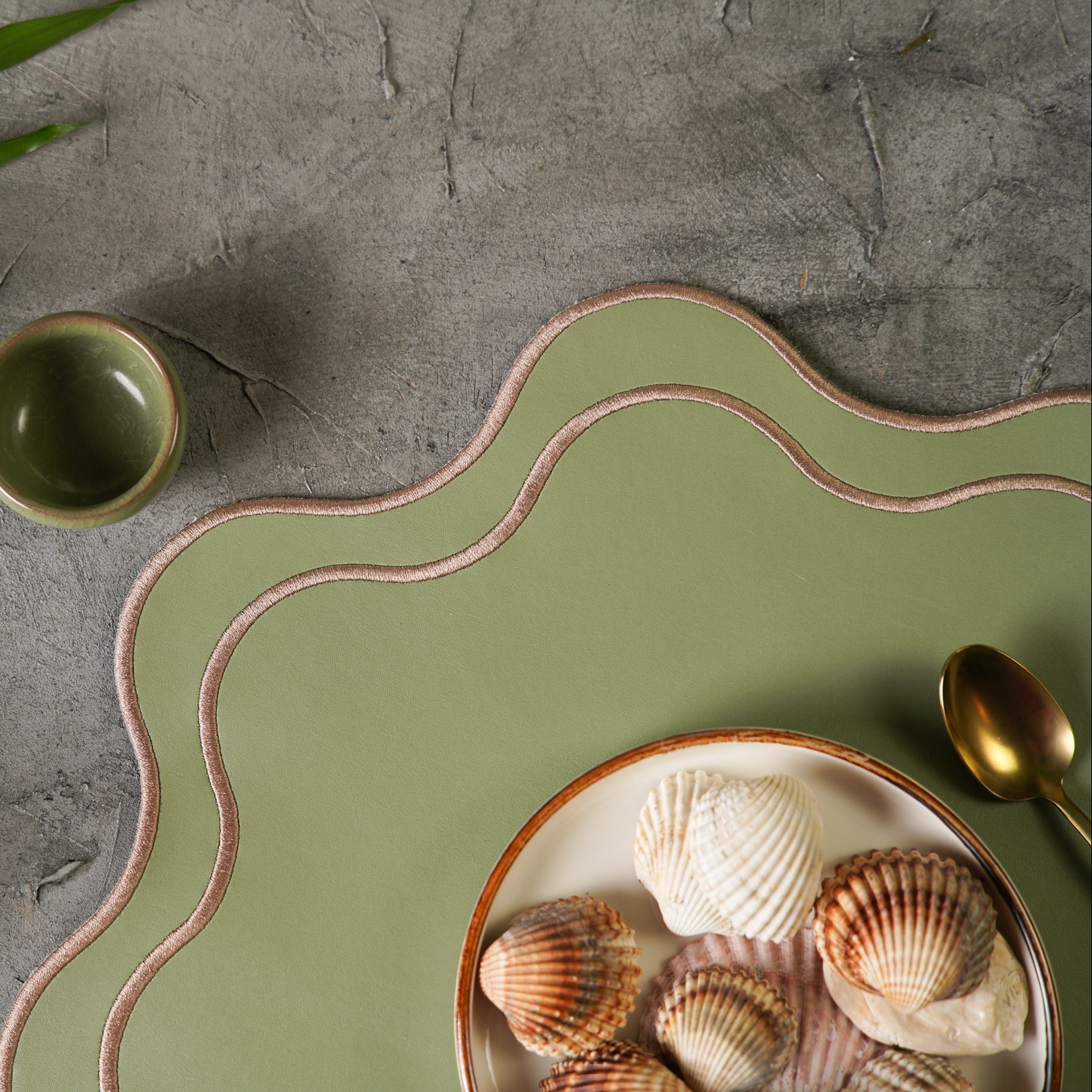 Green ceramic plate with scallop shells on a gray surface with a plant.