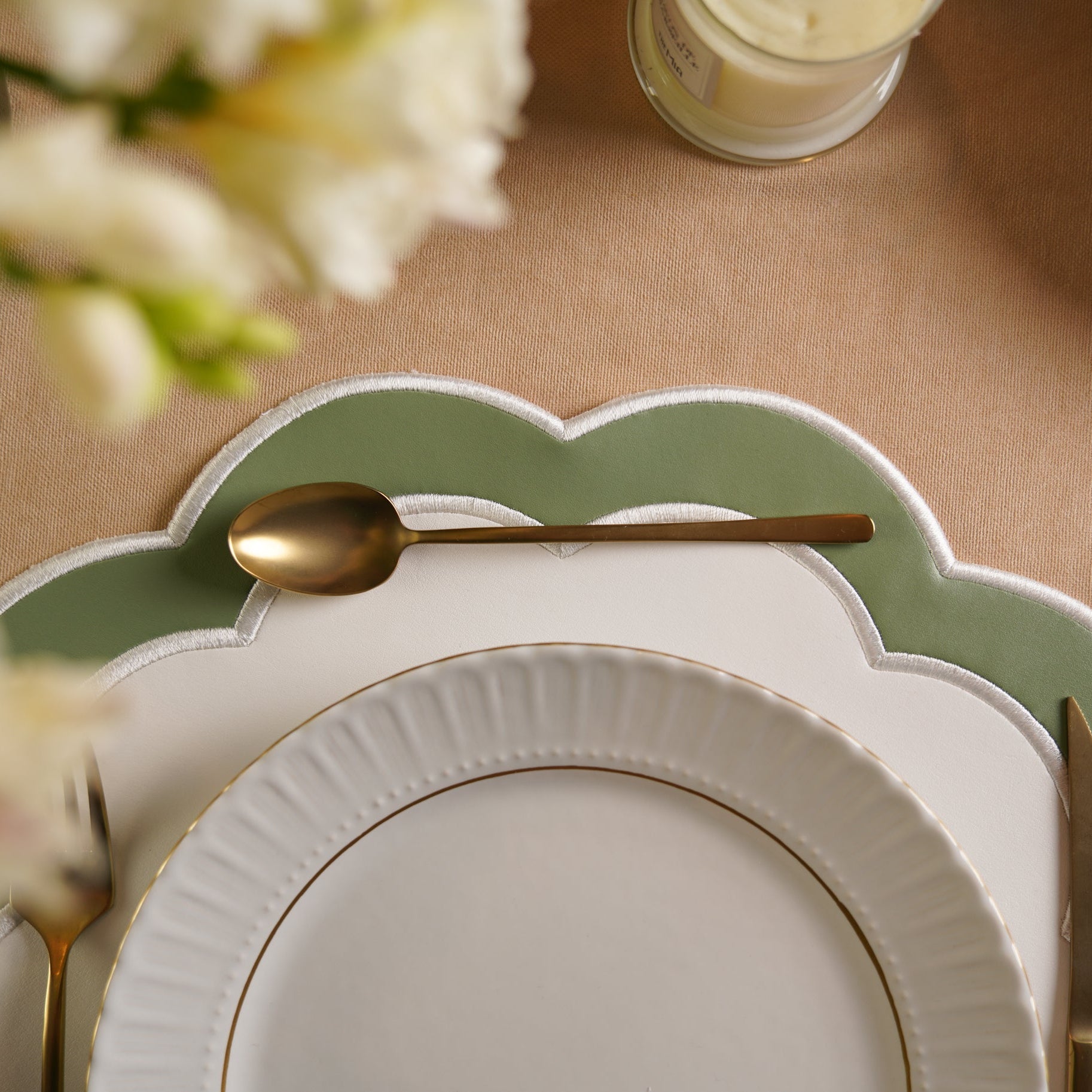 Elegant table setting with white plates, gold spoons, and a green charger plate.