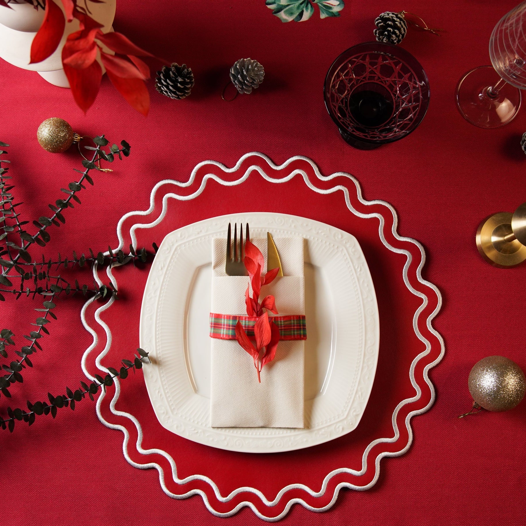 A red faux leather placemat with a decorative border, presented on a table with a white plate and red cutlery.